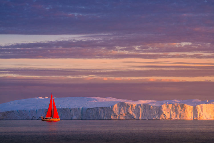 Red Sailboat Next to Iceberg in Disko Bay