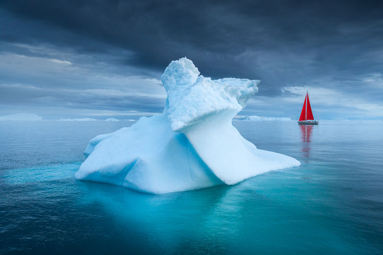 Red Sailboat Next to Iceberg in Disko Bay