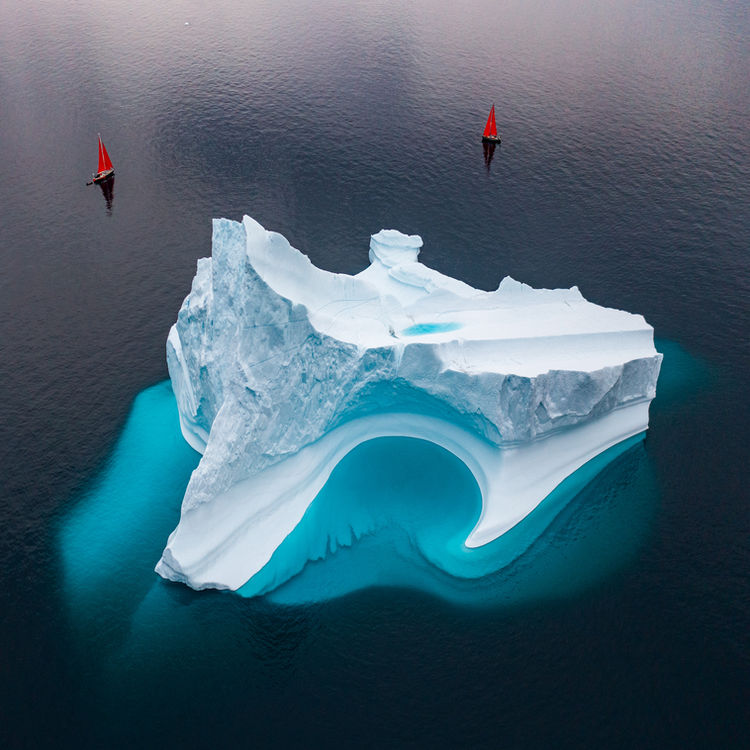 Red Sailboats Around an Iceberg in Greenland