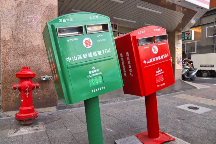 two taiwanese mailboxes bent by a hurricane, one green and one red