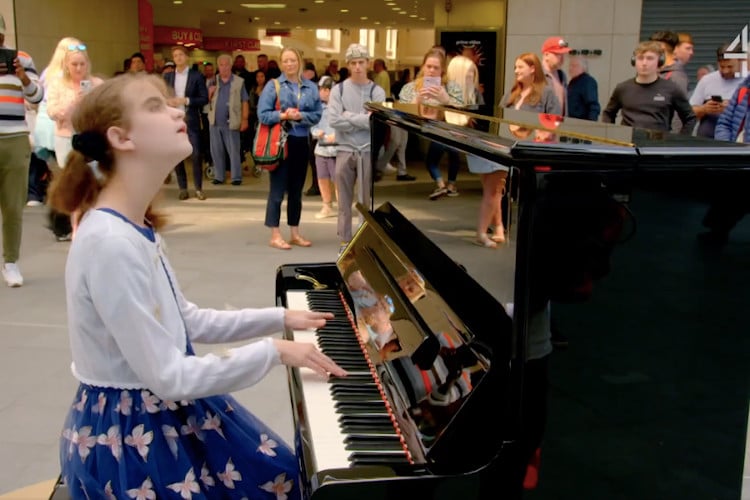 - ViralBandit Lucy, a 13-year-old blind and neurodivergent girl plays the piano, looking like she's enjoying the music she's playing.