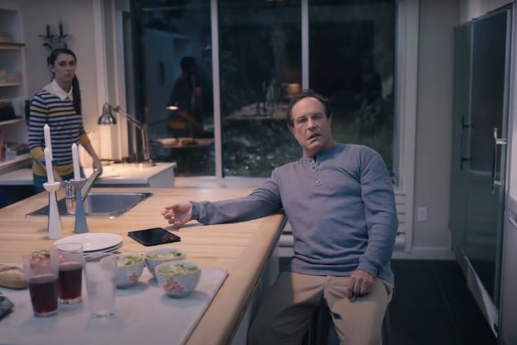 Man sitting and daughter standing in kitchen in screenshot of video about the first signs of a stroke