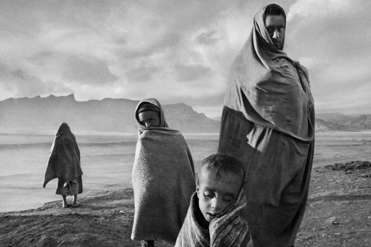 Draped in blankets to keep out the cold morning wind, refugees wait outside Korem camp.