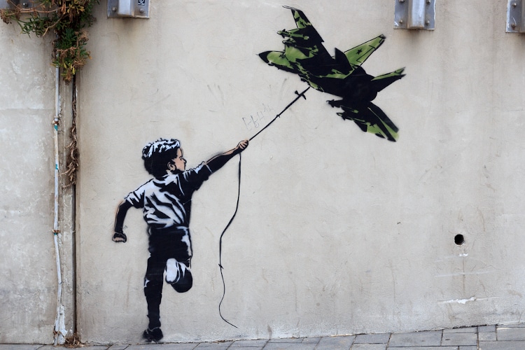 Banksy street art graffiti boy with fighter aircraft kite