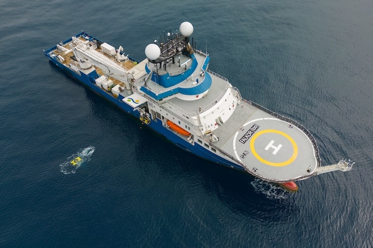 The blue research vessel the Falkor (too) is seen from above in the ocean